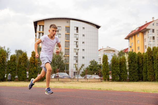 Kid running on the track in the city with buildings behind him. Sprinting.