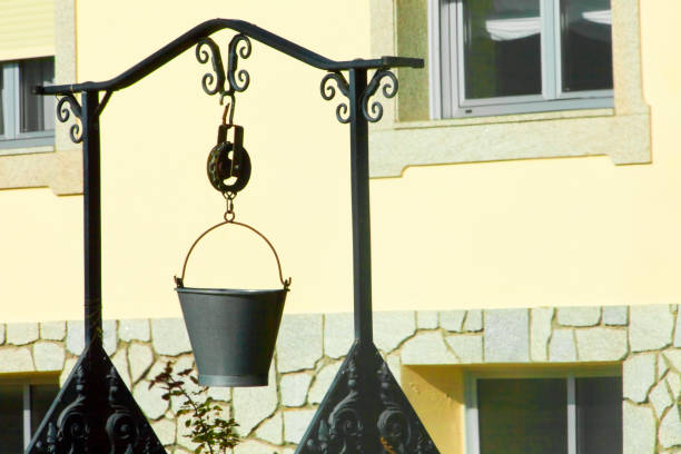 A close-up of a weathered metal bucket filled with water, floating autumn leaves, and a rusty outdoor pump in the background. The composition captures the charm of rural life and the passage of time, accented by the colors of fall. Perfect for themes of nostalgia, countryside, and seasonal transitions.