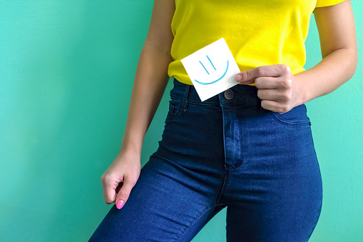 Girl holds a little piece of paper note with happy emoji on it. Concept of healthy stomach and no menstrual cramps