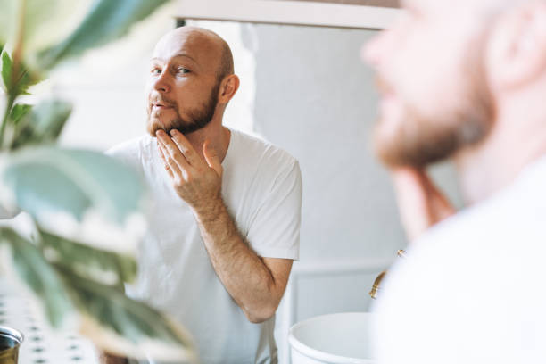 istock Handsome bald man looking at mirror and touching face in bathroom 1412710151