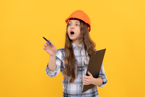 shocked teen girl in helmet and checkered shirt making notes on clipboard, working.
