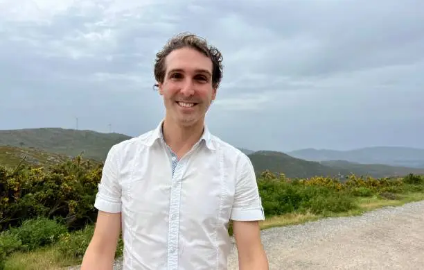 a handsome French or Spaniard man in a white shirt stands against the backdrop of mountains. High quality 4k footage