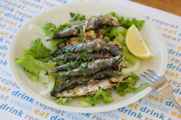 Fresh and crispy fried anchovies served with lemon slices and green leaves salad. Ideal summer bite. stock photo