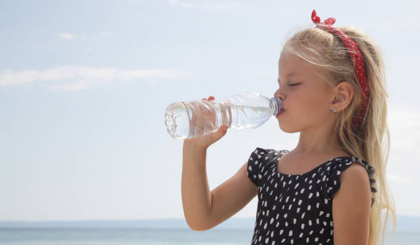 Little girl having water break on the beach to avoid dehydration and heat illness. Concept of keeping children hydrated and safe during a heatwave. stock photo