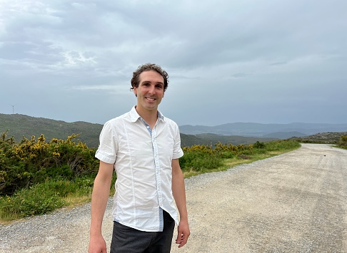 a handsome French or Spaniard man in a white shirt stands against the backdrop of mountains. High quality 4k footage