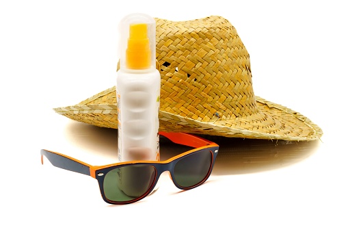 Close-up view of a straw hat, suntan lotion, beach towel and sunglasses. Summer vacations, sun protection and sun safety.