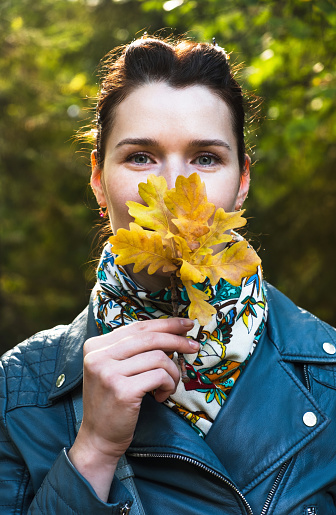 Portrait beautiful young woman with autumn yellow leaves on sunlight park background. Vertical, close up