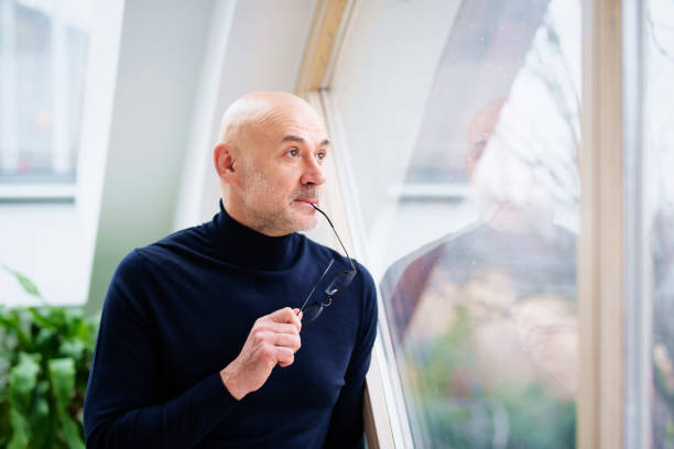 istock Man looking thoughtfully while standing at the window and looking out 1412714483