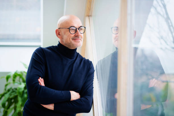 Confident man deep in thought while standing at the window and looking out