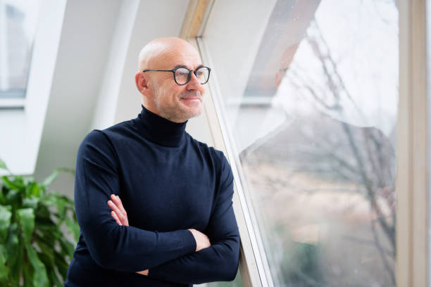 istock Confident man deep in thought while standing at the window and looking out 1412714496
