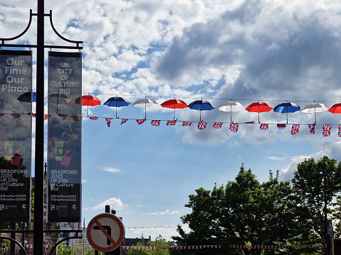 Bradford, United Kingdom - June 3, 2022: Posters promoting Bradford's bid for the 2025 UK City of Culture set against hanging red white and blue umbrellas. The posters are on Market St near the Mirror Pool.
