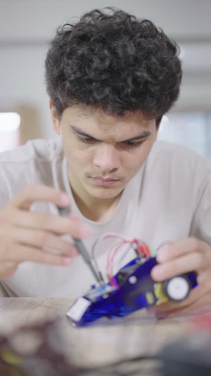 Close-up of a high school boy using screwdriver to repair his robotic car with concentration.