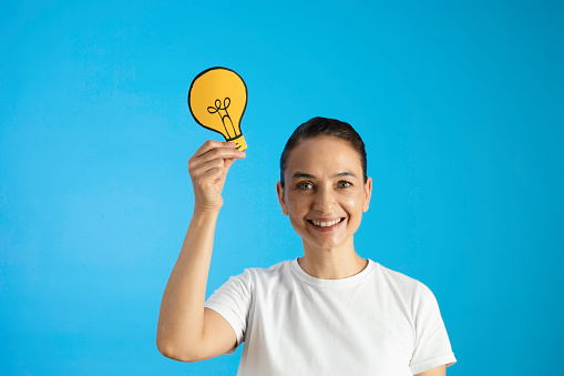 Woman holding light bulb on head against blue background.
