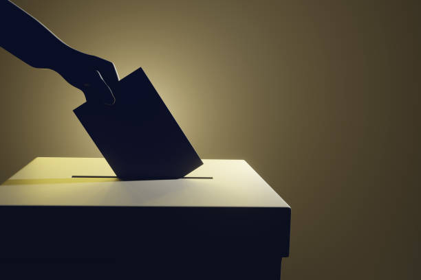 istock Silhouette of a hand putting a vote into the voting box on pale yellow background 1412722623