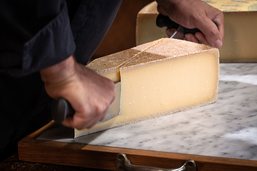 A man cuts a portion of The Gruyère with a wire, the famous swiss cheese in a cellar on a marbble background