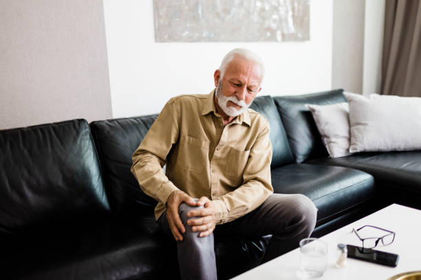 istock A distraught senior man feeling unwell, suffering from pain in leg while sitting on sofa in the living room at home, Photo of  elderly man sitting on a sofa in the living room at home and touching his knee by the pain during the day. Senior man massaging 1412726039