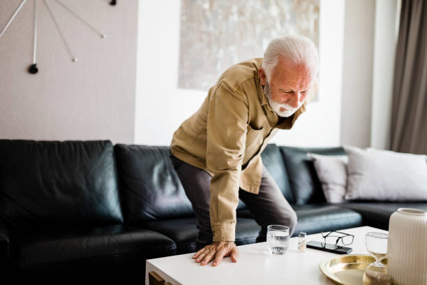 älterer mann fühlt sich unwohl, leidet unter rückenschmerzen, massiert schmerzende muskeln, während er zu hause auf dem sofa im wohnzimmer sitzt. alten- und gesundheitskonzept - arthritis senior adult rheumatoid arthritis sadness stock-fotos und bilder