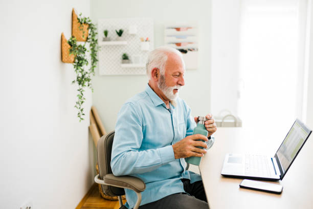 istock Senior man drinking water from reusable bottle at office 1412727378