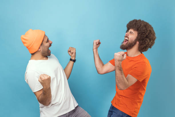 Two men showing yes gesture and screaming celebrating victory, success, dreams comes true. stock photo