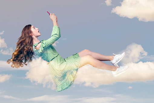 Hovering in air. Surprised shocked girl with mobile phone, chatting online in social network amazed by unbelievable news message, surfing web while flying. collage composition on day cloudy blue sky