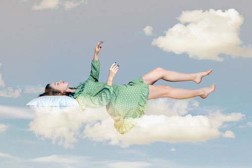 Sleeping beauty floating in air. Relaxed girl in vintage ruffle dress keeping eye closed, lying on pillow levitating, flying in dream with hands up to catch. collage composition on day cloudy blue sky