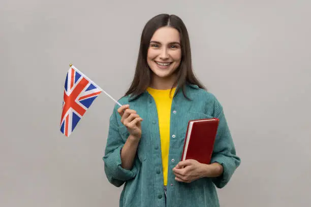 Photo of Clever cheerful woman holding in hands book and british flag, education courses abroad.