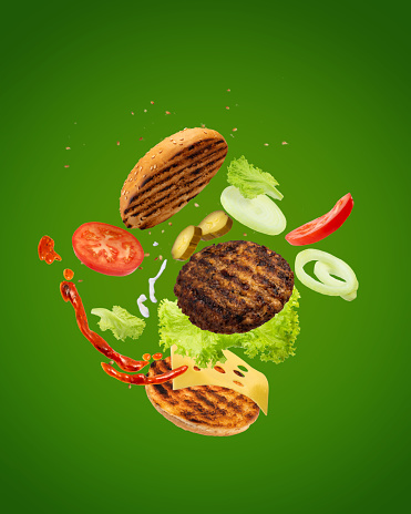 Big tasty hamburger with flying elements. Flying burger. Green background.