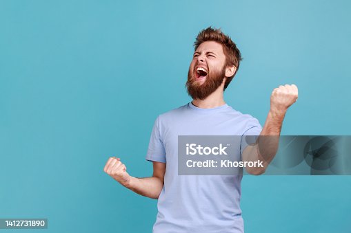 istock Man with excited expression, raising fists, screaming, shouting yeah celebrating his victory success 1412731890
