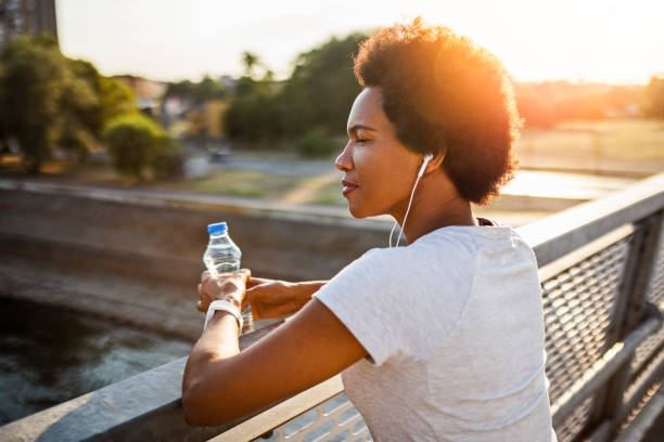 istock Young woman taking a break from jogging across the bridge at sunset 1412737757