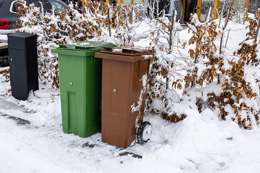 Close up view of house mail post box and waste and recycling containers on snowy bushes background. Sweden.