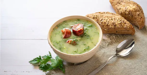 Portuguese style soup called Caldo Verde with traditional bread on a white wooden Table. Copy space