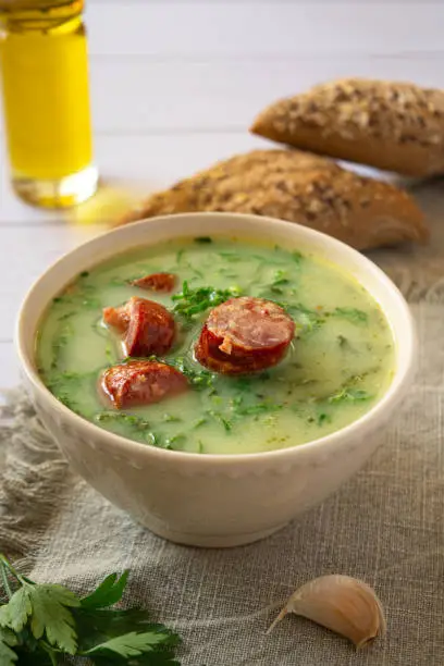 Portuguese style soup called Caldo Verde, bread, oil and garlic on white wooden Table.