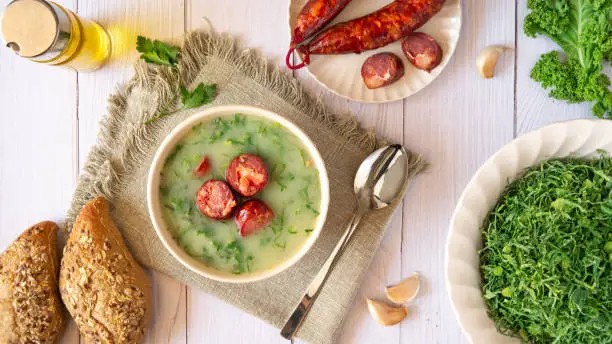 Table with Portuguese-style soup called Caldo Verde and bread, Cabbage julienne, oil, and chorizo sausage. Flat lay