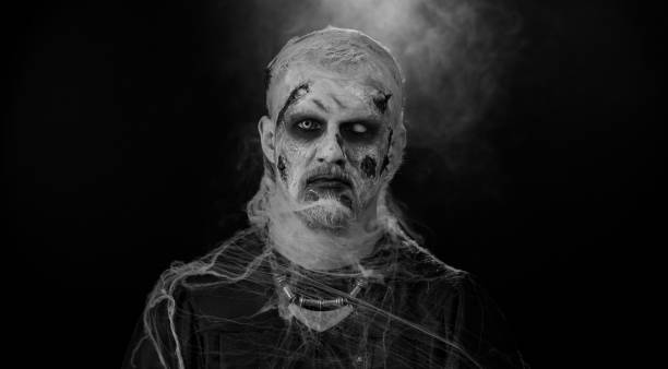 istock Sinister devil man with scary Halloween dead zombie makeup in costume making faces, trying to scare 1412746693