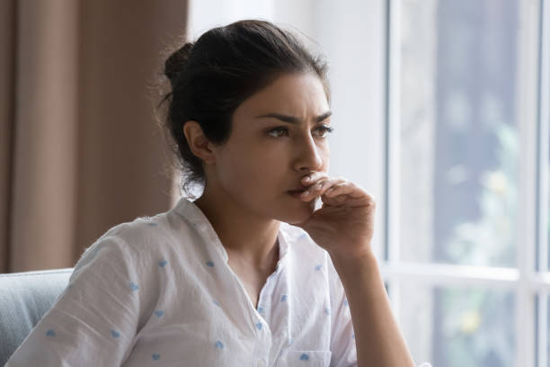 ernsthafte nachdenkliche schöne indische frau, die drinnen auf der couch sitzt - pensive stock-fotos und bilder