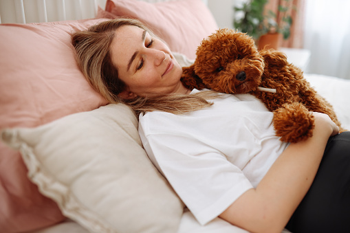 Morning in bed - A young beautiful woman enjoys a non-working day and plays with her dog in bed. Bed sheets.