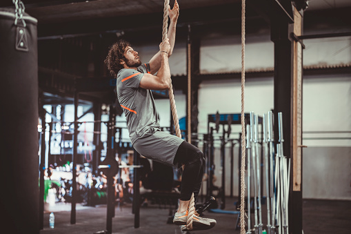 Handsome male athlete climbing up rope for strength training session.