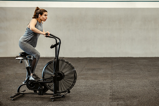 Women using fitness bicycle machine for muscle build, cardio and endurance workout equipment