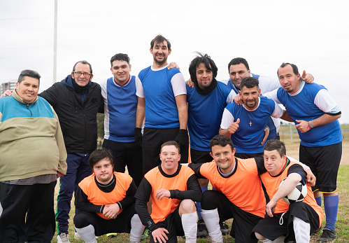 Portrait of some happy mentally disabled soccer players at the field with their coach