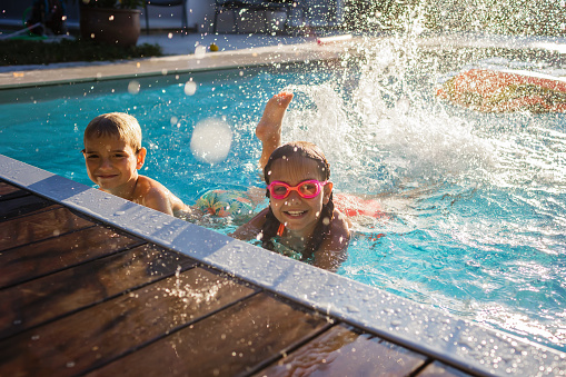A group of five multi-ethnic children, 6 to 9 years old, having fun in a swimming pool, hanging on the edge, kicking as splashing. The girl on the right and the boy in the middle are both mixed race African-American and Caucasian. The Asian girl is Japanese and Filipino.