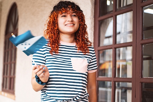 Portrait of a young latin american woman with colorful hair looking away and holding and waving a small honduras flag.