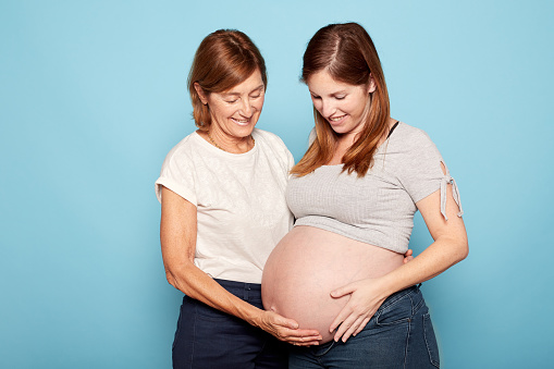 Pregnancy concept. Senior mother and daughter smiling touching pregnant belly