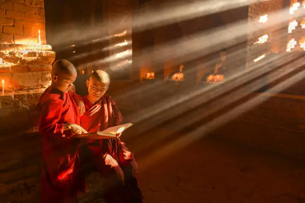 Photo of Two young buddhist monks praying inside the temple in Bagan, Myanmar