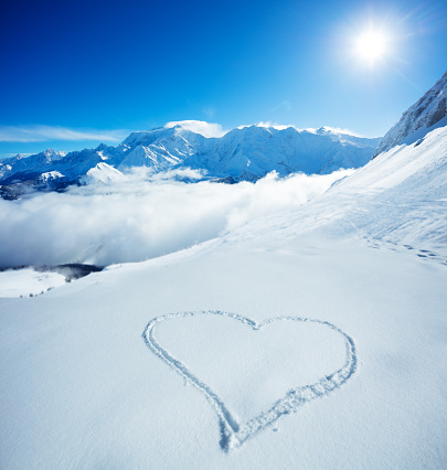 Heart symbol drawn in the snow high in the mountain with snowy Alpine peaks on background