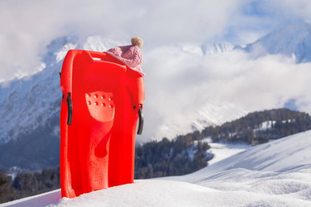 istock Red sledge in snow over the mountain with pink kids hat 1412772583