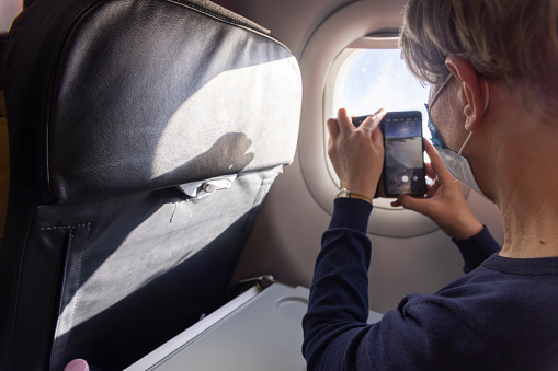 Mature Caucasian women making video from airplane window during the flight.
