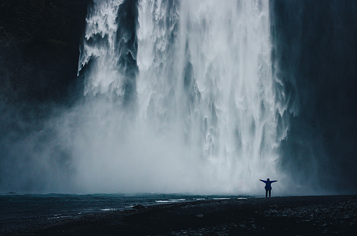 A figure stands in awe before an epic waterfall