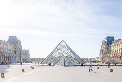 A lot of tourists walk in square of Louvre Museum Pyramid in Paris, France