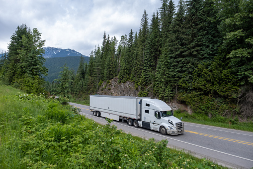 Large container truck driving along a highway. Lush forests and flowing rivers while driving along the Trans Canadian Highway in British Columbia, Canada.