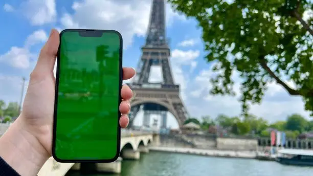 Photo of Phone with green Chromate screen on the background of the eiffel tower. in Paris using her cell phone in front of Eiffel Tower, seine bridge background,